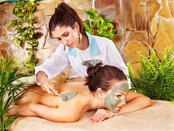 Girl having clay body mask apply by beautician.