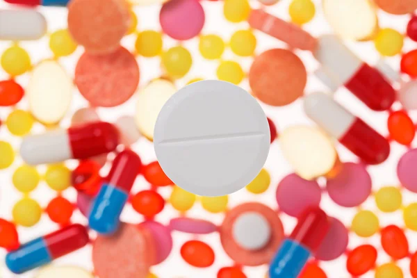 One big tablet (pill) macro view on blurred multicolored drugs b