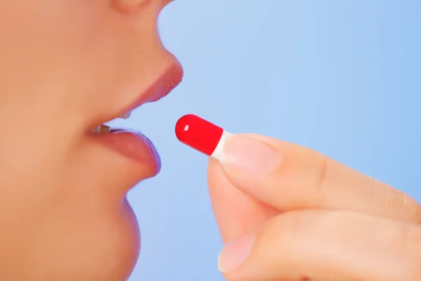Young woman taking red and white bolus (capsule), macro view