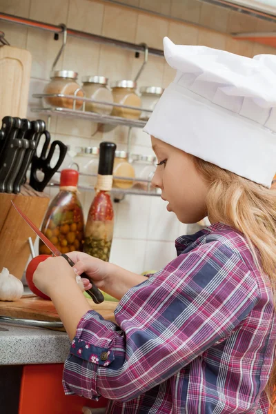 Girl in a chef cap helps to make a dinner.