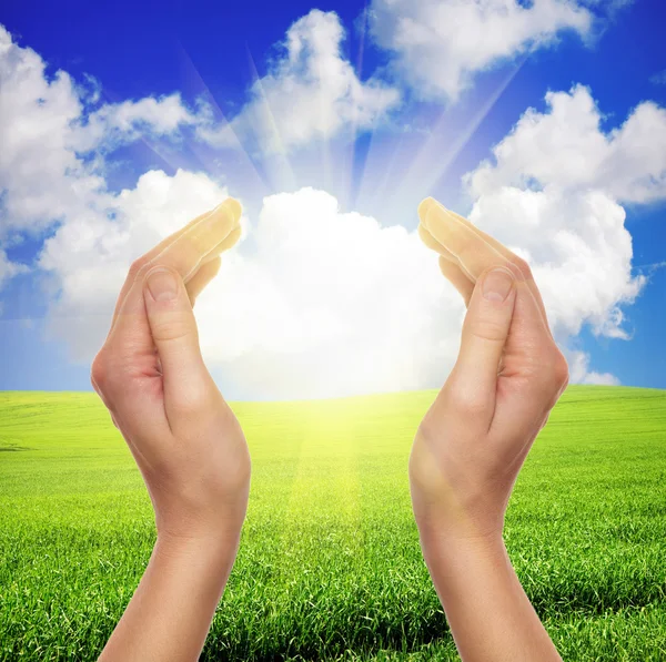 Female hands holding sun over green field of grass and blue sky