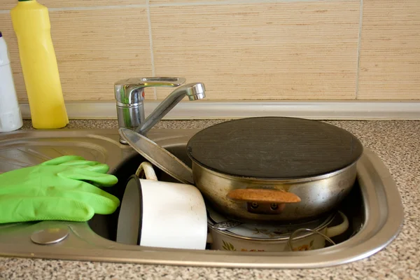 Pile of dirty dishes like plates, pot and cutlery in the sink