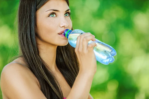 Woman with bare shoulders drinks from bottle of water