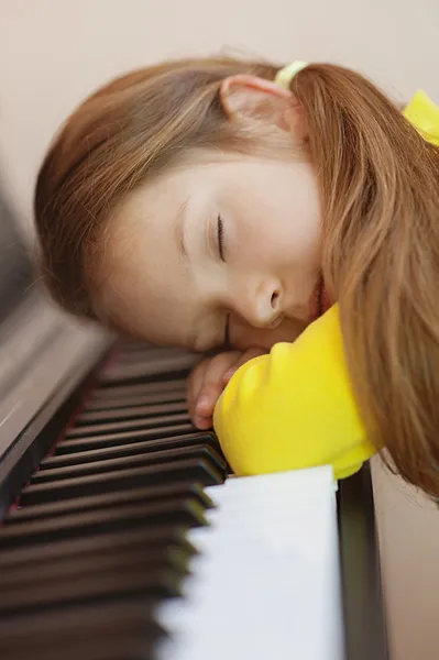 Little girl in yellow dress asleep on piano