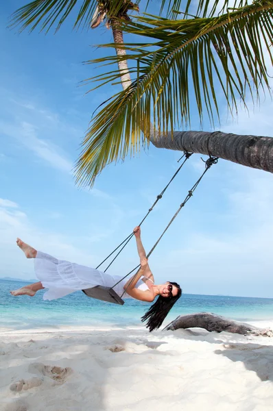 Young woman on the swing on the beach in white dress