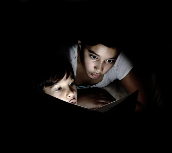 Brother and sister reading light book at night