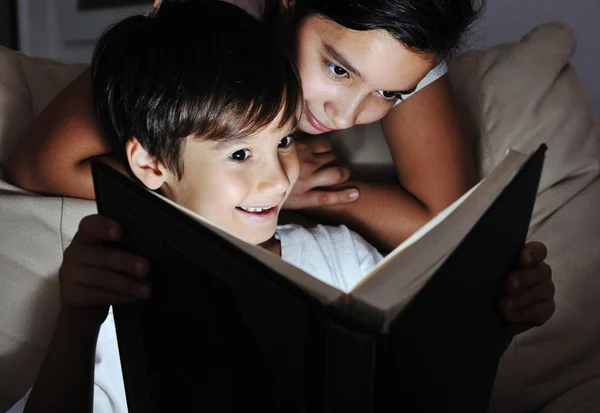 Boy and girl reading light book at night, children concept