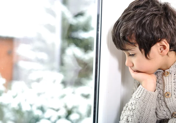 Sad kid on window cannot go out because of cold and snow