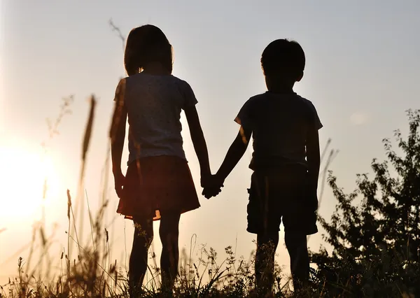 Two children, male and female standing against the sun, sunset, romance