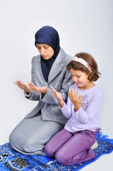 Young muslim woman praying on traditional way with her daughter