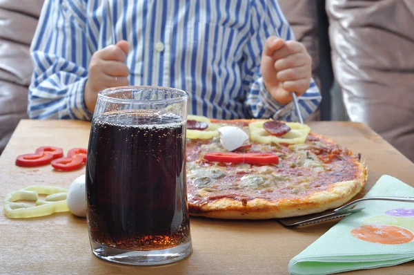 Soda and pizza on table and child in background