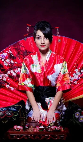 Woman in red Asian costume arranging Japanese tea ceremony