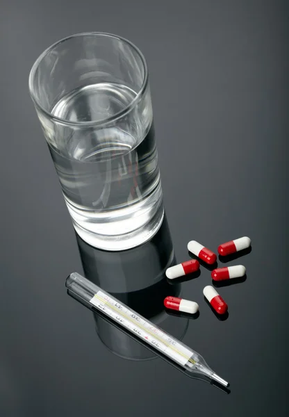 Pills, thermometer and glass of water over dark background