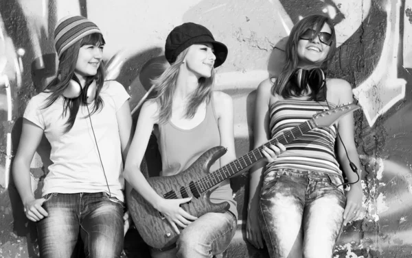 Three beautiful girls with guitar and graffiti wall at backgroun
