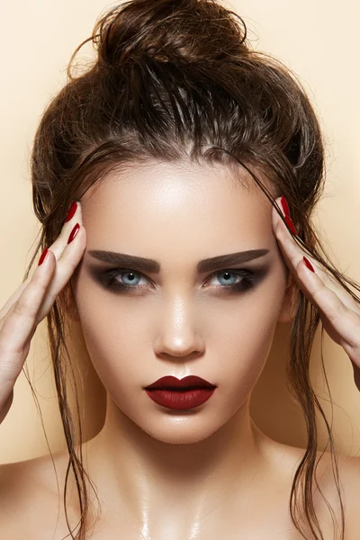 Hot young woman model with sexy dark red lips makeup, strong eyebrows, clean shiny skin and wet bun hairstyle. Beautiful fashion portrait of glamour female face