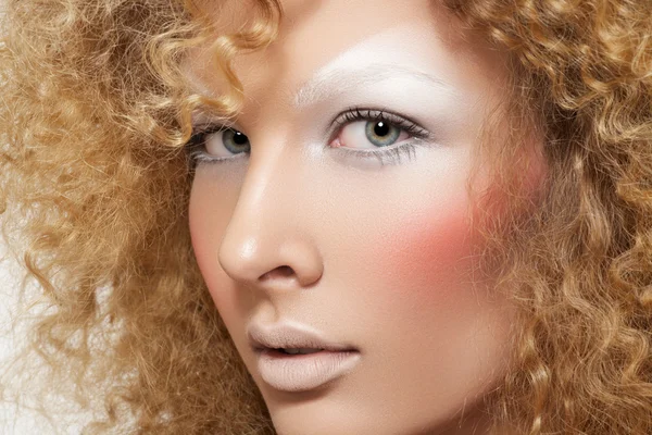 Lovely model with shiny volume curly hair, winter white eyeshadows make-up, pale lips and pink cheeks. Christmas look with frizzy hairstyle