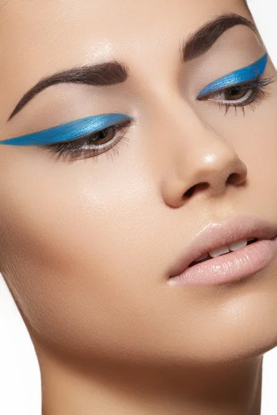 Glamour close-up portrait of beautiful woman model face with winged bright blue eyeliner make-up, clean skin on white background