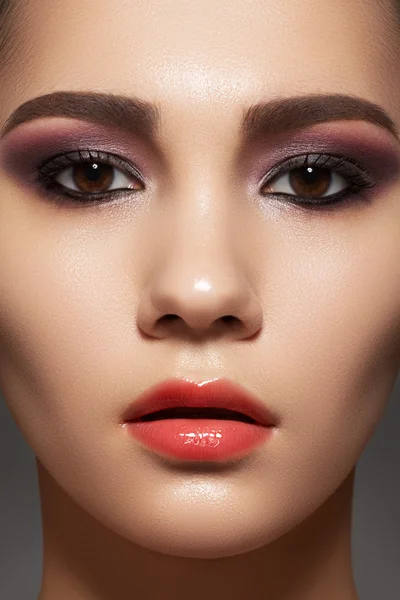 Closeup beauty portrait of attractive model face with bright visage. Purple eye makeup and gloss lips make-up