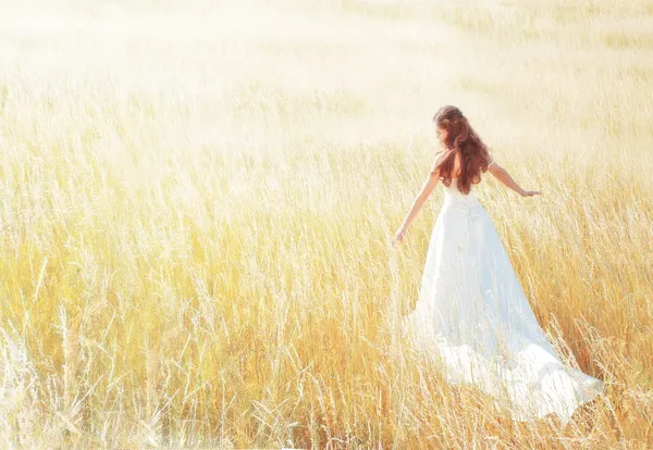 Woman walking in the sunny meadow on summer day touching grass