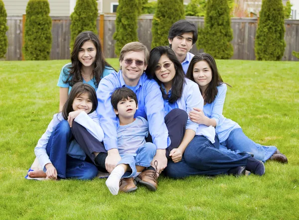 Large family of seven sitting together on lawn, dressed in blue