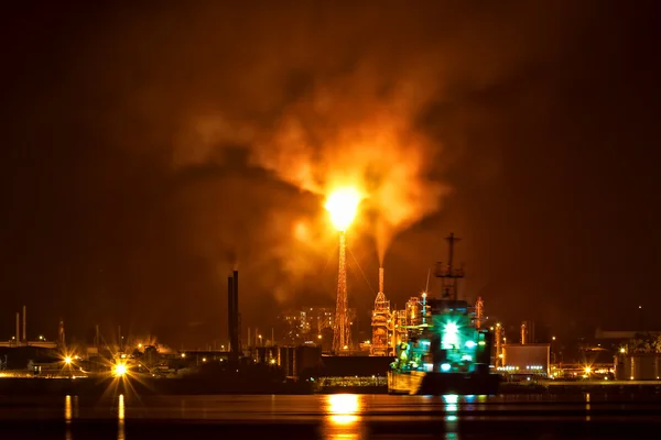 Oil refinery at night polluting the air with a huge smoke column