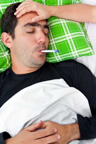 Sick hispanic man laying in bed with a thermometer