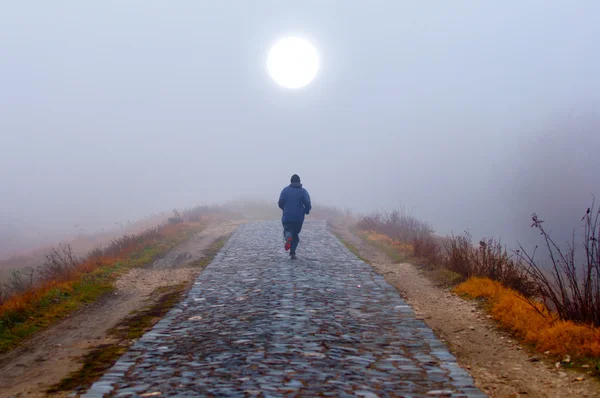 Lonely man running toward the sun on misty autumn morning