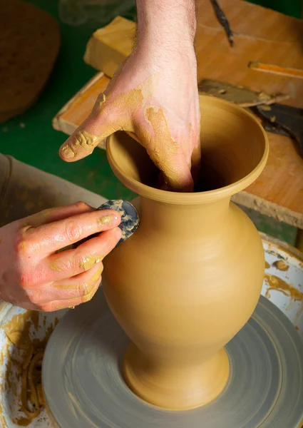 Craftsman making vase from fresh wet clay on pottery wheel.