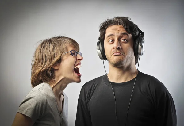 Angry wife screaming against her husband not listening to her wearing headphones