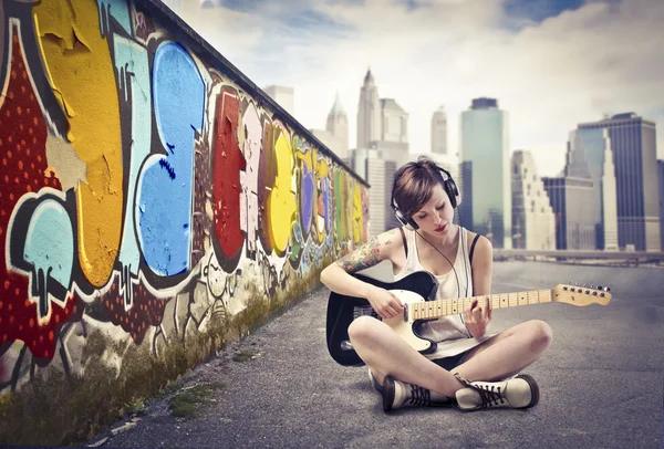 Beautiful young woman sitting on a city street and playing the electric guitar