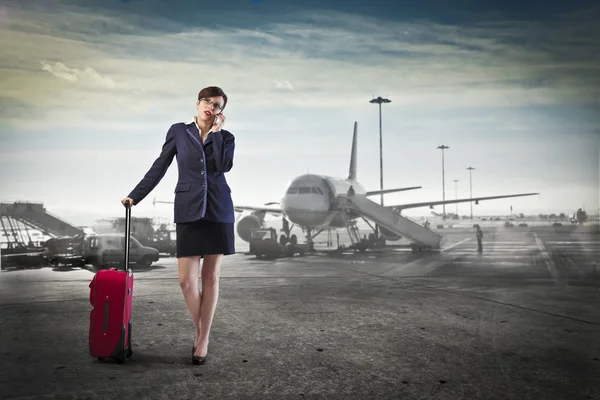 Young businesswoman at the airport holding a trolley case and talking on the mobile phone