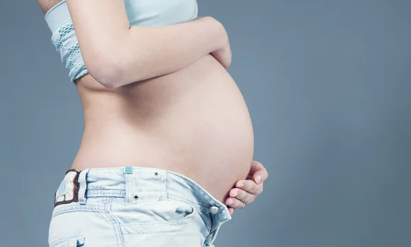 Closeup of belly with hands on it. Pregnant white woman wearing light blue top and jeans. Pregnancy collection.