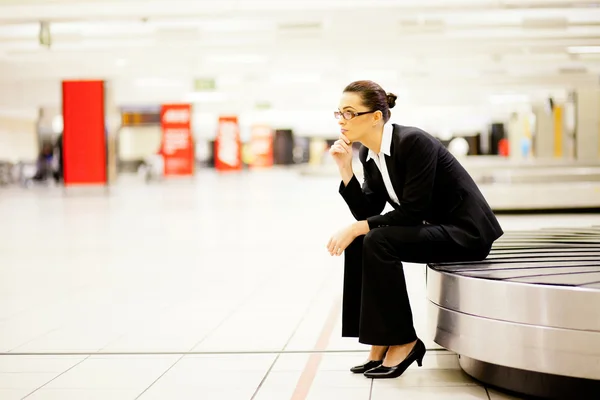 Businesswoman sitting on conveyor belt and waiting for her luggage