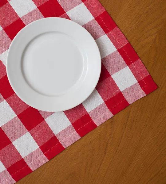 White plate on wooden table with red gingham tablecloth
