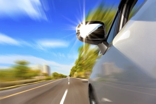 Car on the road with motion blur and sunlight in the mirror