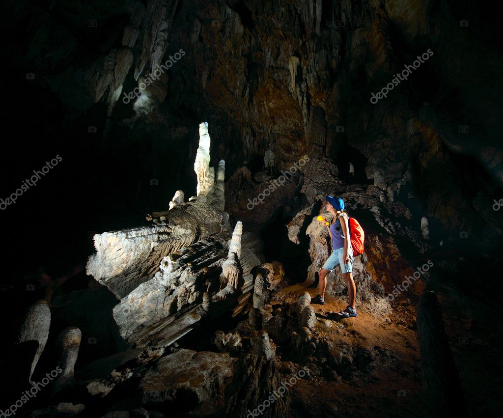 Young woman with backpack exploring huge cave with torch