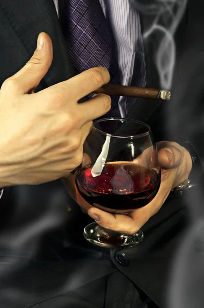 Old Brandy Glass at male hand, smoking cigar