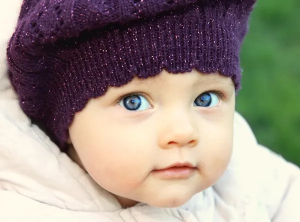 Funny baby in hat with big blue eyes looking on nature green back
