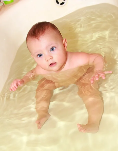 Adorable baby girl swimming in the bath sitting and looking funny