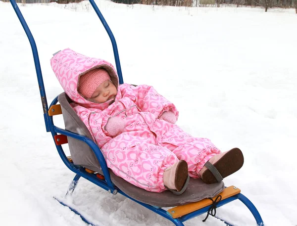 Beautiful baby girl in pink warm dress sleeping on sleigh on win — Stock Photo #9239798