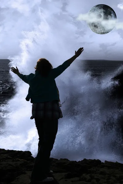 One woman with raised hands facing a wave and full moon on cliff