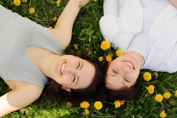 Two beautiful young girls lie side by side on the grass