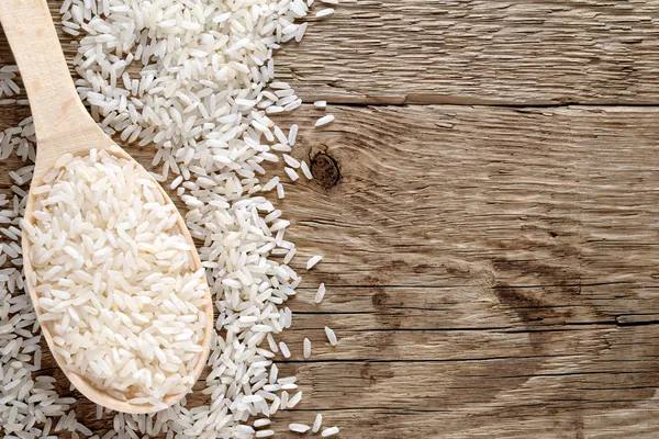 Raw white rice in spoon on wooden background
