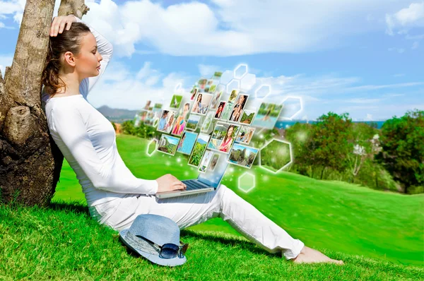 Pretty woman sitting by tree with laptop computer