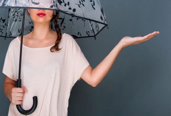 Young fashionable woman holding umbrella standing against grey b
