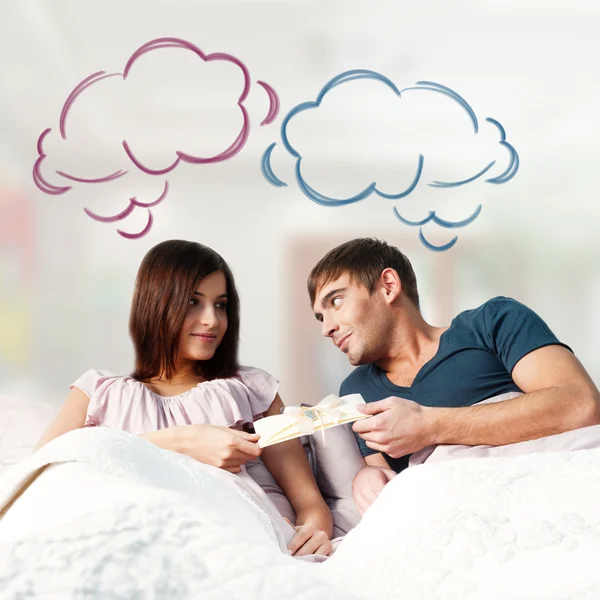 Close-up portrait of adult couple lying on their bed at their apartment and man giving a greeting card to his girlfriend. Blank balloon at the top of the photo for your text. Planning future concept