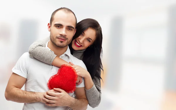 Portrait of young couple with red heart standing at their home and embracing