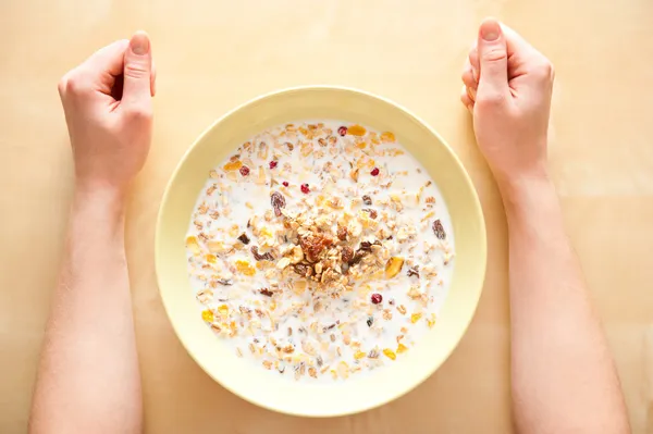 Cereal muesli breakfast with dried fruit and nuts and milk and woman hands on table. Top View