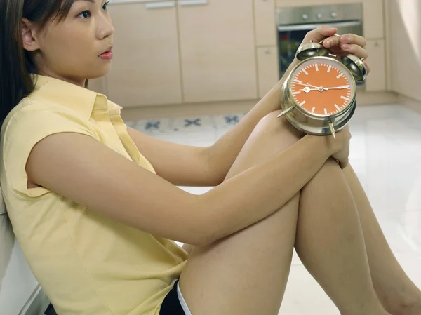 A woman waiting for her laundry while holding a clock
