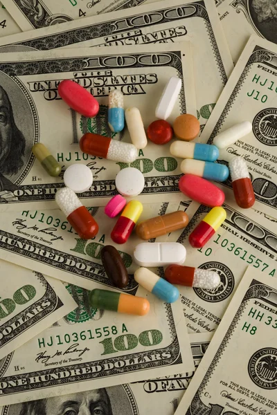 Pills of different colors on money background.